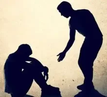 A person is trying to to help other person who is addict and sad sitting with his head down, worrying about his life and how to overcome addiction to achieve recovery.